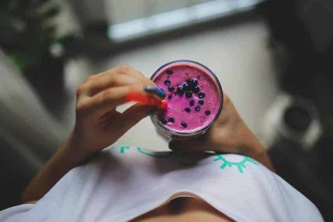 Hands holding a glass of purple smoothie topped with blueberries, representing healthy probiotic supplements.
