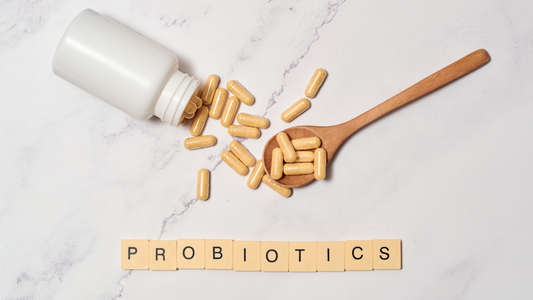 Prebiotic supplement capsules spilling from white bottle with wooden spoon and probiotic word tiles on marble surface