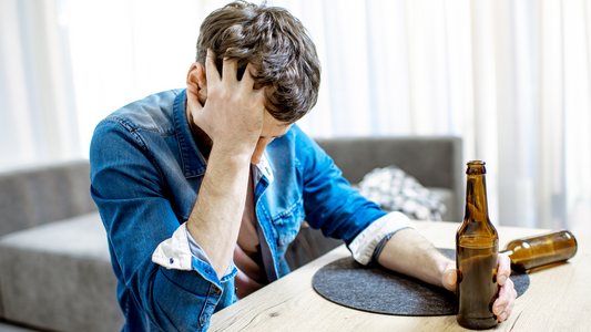 man struggling with alcoholism disease holding beer bottle at home feeling distressed