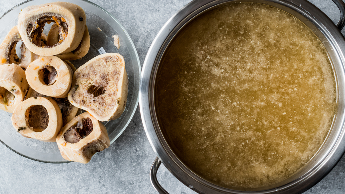 Bone broth in pot with beef marrow bones on plate, foods to improve a leaky gut nutrition