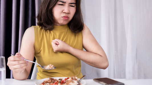Woman in yellow shirt experiencing heartburn while eating food at table as effective way to treat heartburn concept