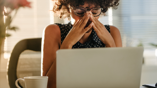 Stressed woman massaging nose bridge in front of laptop highlighting stress affects gut health concept