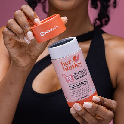 Woman holding Her-Biotics Sport Capsules probiotic multivitamin bottle with orange cap, designed for active women
